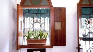 Una finestra con cornice in legno e inferriata, attraverso cui si intravede una pianta in vaso.