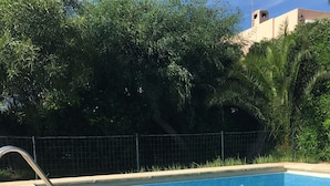 En klar, blå swimmingpool med en metalstige til venstre, omgivet af en betonflisebelagt terrasse.