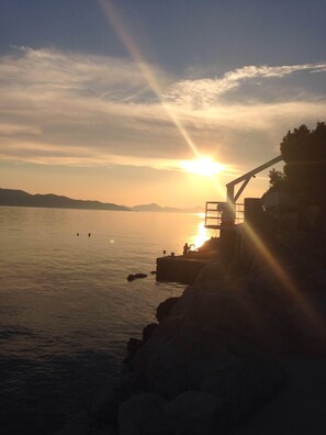 A sunset over a calm body of water with a rocky shoreline and a structure with a viewing platform.