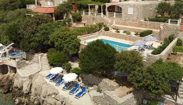 A stone pool surrounded by trees, with lounge chairs and umbrellas.