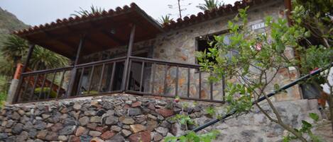 A stone house with a tiled roof, a balcony with metal railings, and a stone wall.