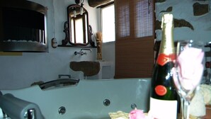 Een badkamer met een badkuip, een spiegel en een fles champagne op een tafel.