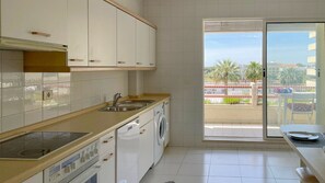 A modern kitchen with a built-in oven, a washing machine, and a large window offering a view of palm trees and buildings.