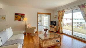Un salon avec un canapé, une table basse en verre, un téléviseur et un balcon agrémenté de rideaux.