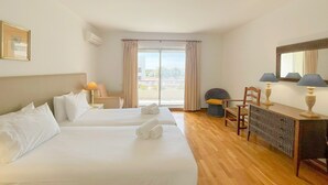 Une chambre d’hôtel avec deux lits, un bureau, une chaise et une grande fenêtre avec des rideaux.
