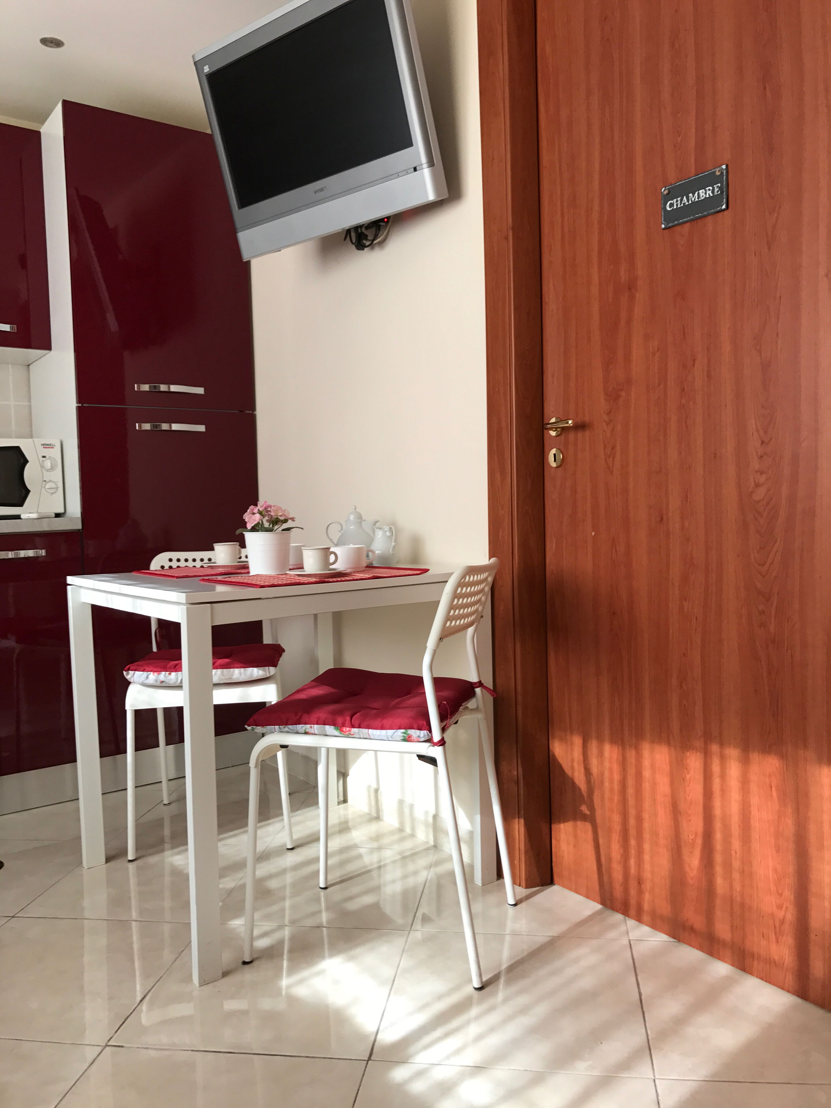Ein Essbereich mit Tisch, Stühlen, einem an der Wand montierten Fernseher und einer Tür mit der Aufschrift 'CHAMBRE'.