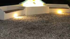 A hot tub with a curved design, surrounded by gravel, under a night sky with visible moon and stars.