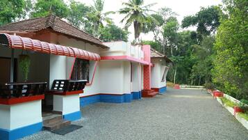 A row of two-story buildings with red and blue trim, a gravel pathway, and lush greenery in the background.