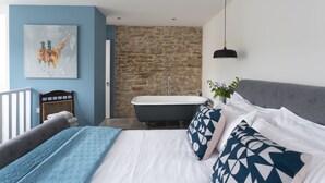A modern bedroom with a bed, a painting, a bathtub, and a grey headboard. - The Garden Rooms @ Drumagosker Rural Retreats (Limavady)