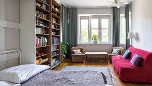 Une chambre à coucher avec un lit, un canapé rouge, une bibliothèque, une fenêtre avec des rideaux et un ventilateur de plafond.