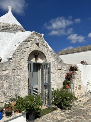 A stone building with a conical roof, a door, and potted plants.