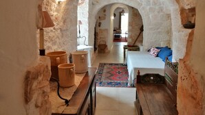 A rustic room with a stone archway, a bed with a patterned bedspread, a wooden bench, and a small table with a lamp. - Trullo holiday house Apulia with above ground pool (Ceglie Messapica)