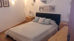 Quarto com cama, mesa de cabeceira, cômoda e decorações na parede, incluindo quadros e um enfeite em formato de coração.