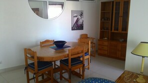 Uma sala de jantar com uma mesa redonda de madeira e cadeiras, uma tigela azul e um armário de madeira com prateleiras.