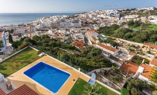 Vista aérea de uma cidade costeira com uma grande piscina cercada por vegetação e edifícios residenciais.
