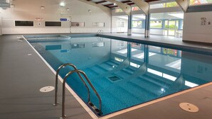 Une piscine intérieure dotée d’un haut plafond, de murs en verre transparent et d’un sol carrelé.