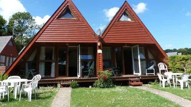 Un bâtiment en bois de forme triangulaire et symétrique, doté de grandes fenêtres et d’un espace porche.