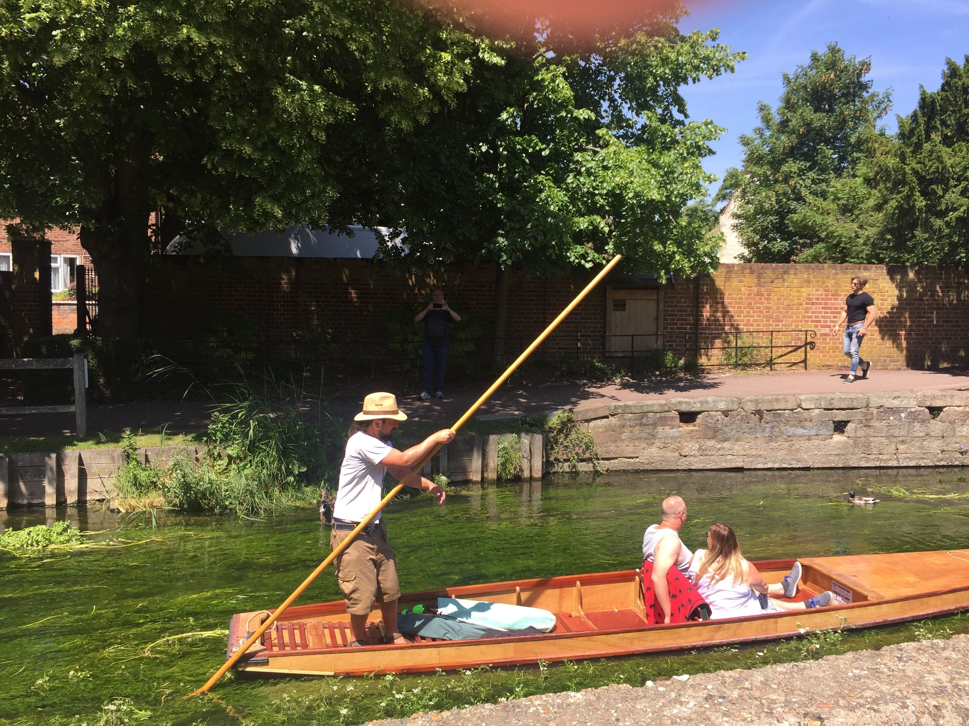 A narrow waterway with a wooden boat carrying two passengers and a guide.