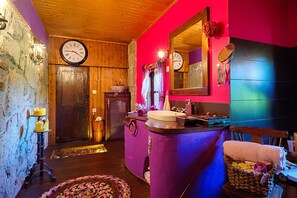 A bathroom with wooden walls, a purple sink vanity, a mirror, and a clock on the wall.