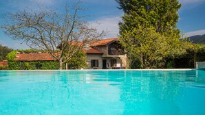 En klarblå pool med en byggnad av sten och frodig grönska i bakgrunden.