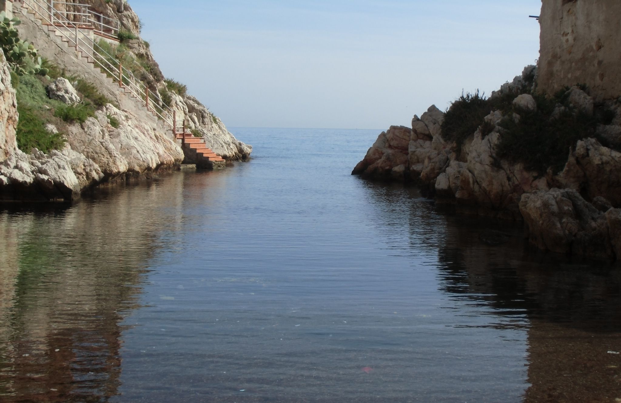 A narrow waterway flanked by rocky cliffs with a staircase leading up.