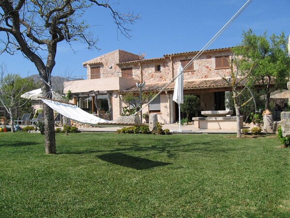 A stone building with a tiled roof, a hammock, and a stone fountain in the yard. - Villa With Private Pool, Sauna And Jacuzzi (Pollença)