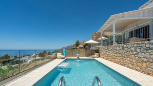 En swimmingpool med kristallklart blått vatten, stenmurar och utsikt över havet.