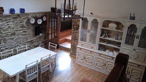 Zona pranzo con parete in pietra, tavolo bianco e sedie. Si vede una scala che conduce a un piano superiore.