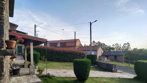 Un vialetto in pietra conduce a una casa rustica con una porta verde, circondata da siepi curate e vasi di piante.