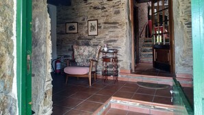 Una stanza rustica con pareti in pietra, una scala in legno, una sedia e un piccolo tavolo con una bottiglia.