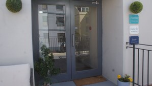 A building entrance with a glass door, a small potted plant, and a doormat. - Central Sidmouth studio apartment with Sea Peeps (Sidmouth)