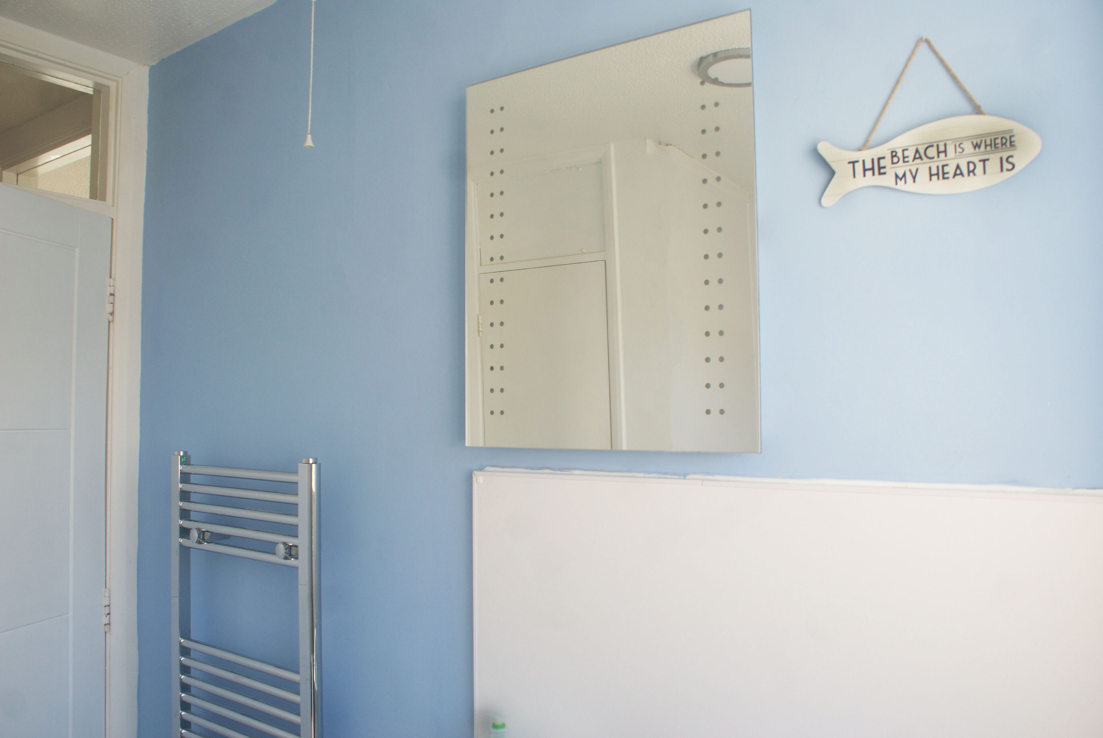 Une salle de bain équipée d’un porte-serviettes, d’un miroir et d’un panneau fixé au mur.