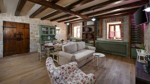 Un intérieur rustique avec des poutres apparentes, des murs en pierre, un meuble vert, un canapé et une table à manger.