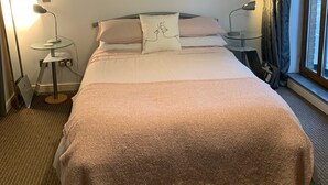 Una habitación de hotel con cama, un cuadro en la pared, una ventana con cortinas y una lámpara en una mesita de noche.