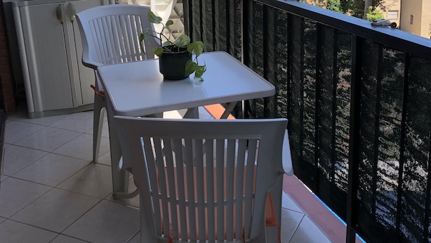 Un balcon avec une table et des chaises, des plantes en pot et une vue sur la mer et les bâtiments.