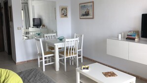 Un salon moderne comprenant un coin repas, des meubles blancs, un téléviseur et une bibliothèque.