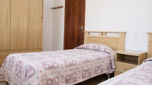 Ein Schlafzimmer mit zwei Einzelbetten, Holzschränken, einem Nachttisch aus Holz und einer Steckdose.