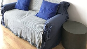 Una habitación con un sofá a rayas, dos almohadas azules y una mesa redonda. Hay tres cuadros enmarcados en la pared.