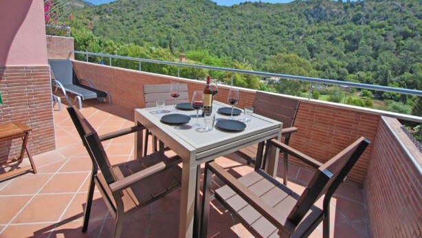 A terrace with a table set for dining, surrounded by brick walls and a scenic view of a forested hill.