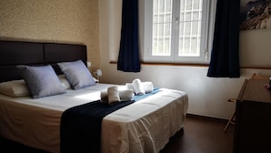 A neatly made bed with white linens and a blue throw blanket, a headboard, and a window with curtains.