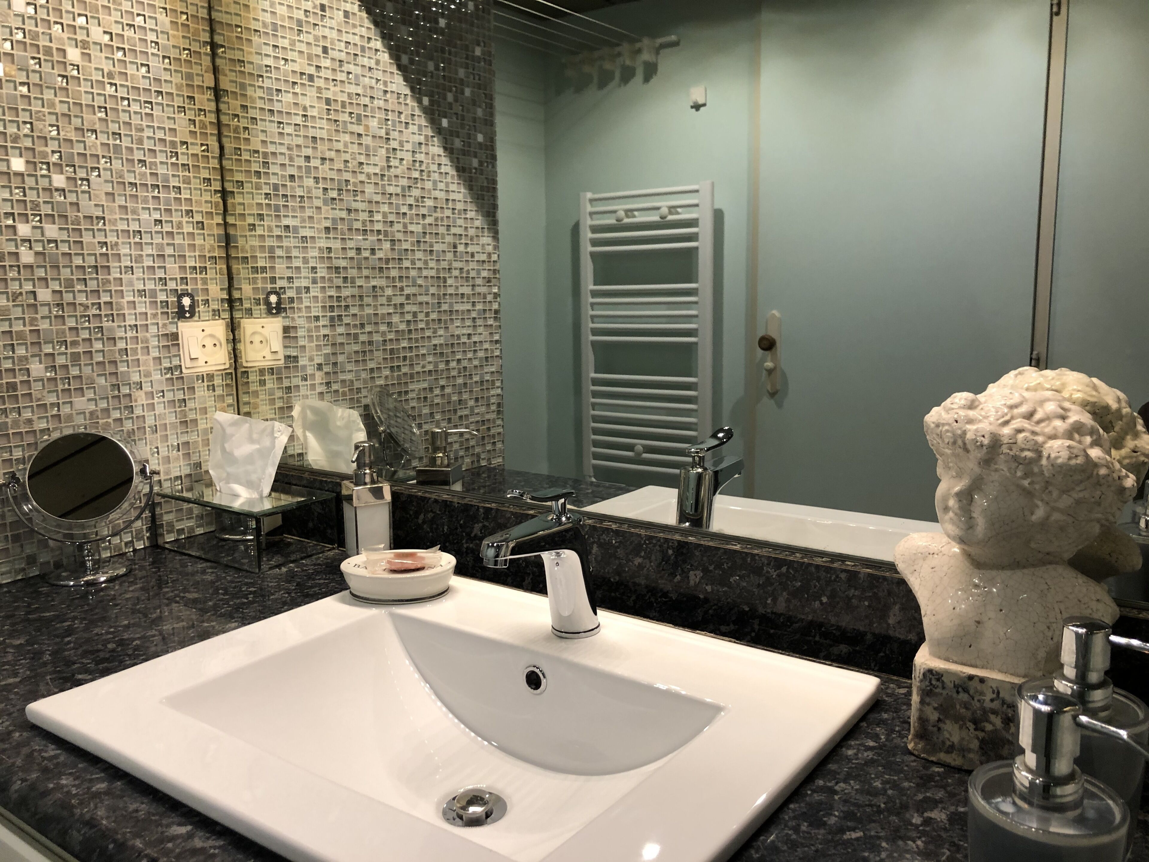 A bathroom with a white sink, a mirror, a towel rack, and a decorative bust.