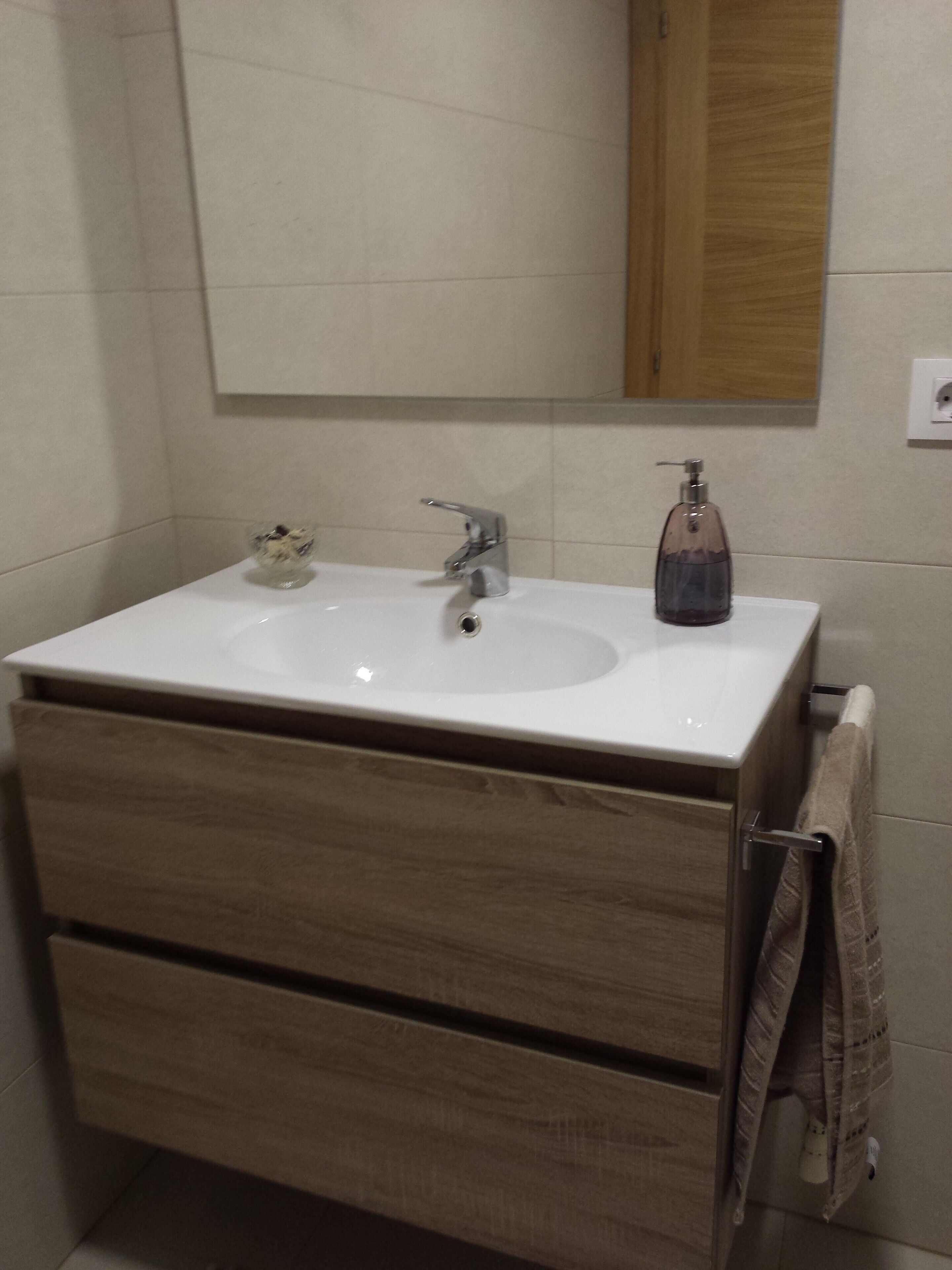 A bathroom with a white sink, wooden vanity, and a towel hanging on the wall.