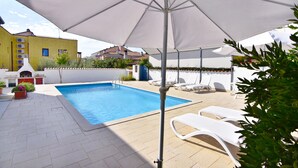 Una piscina con un ombrellone bianco, lettini e piante in vaso.