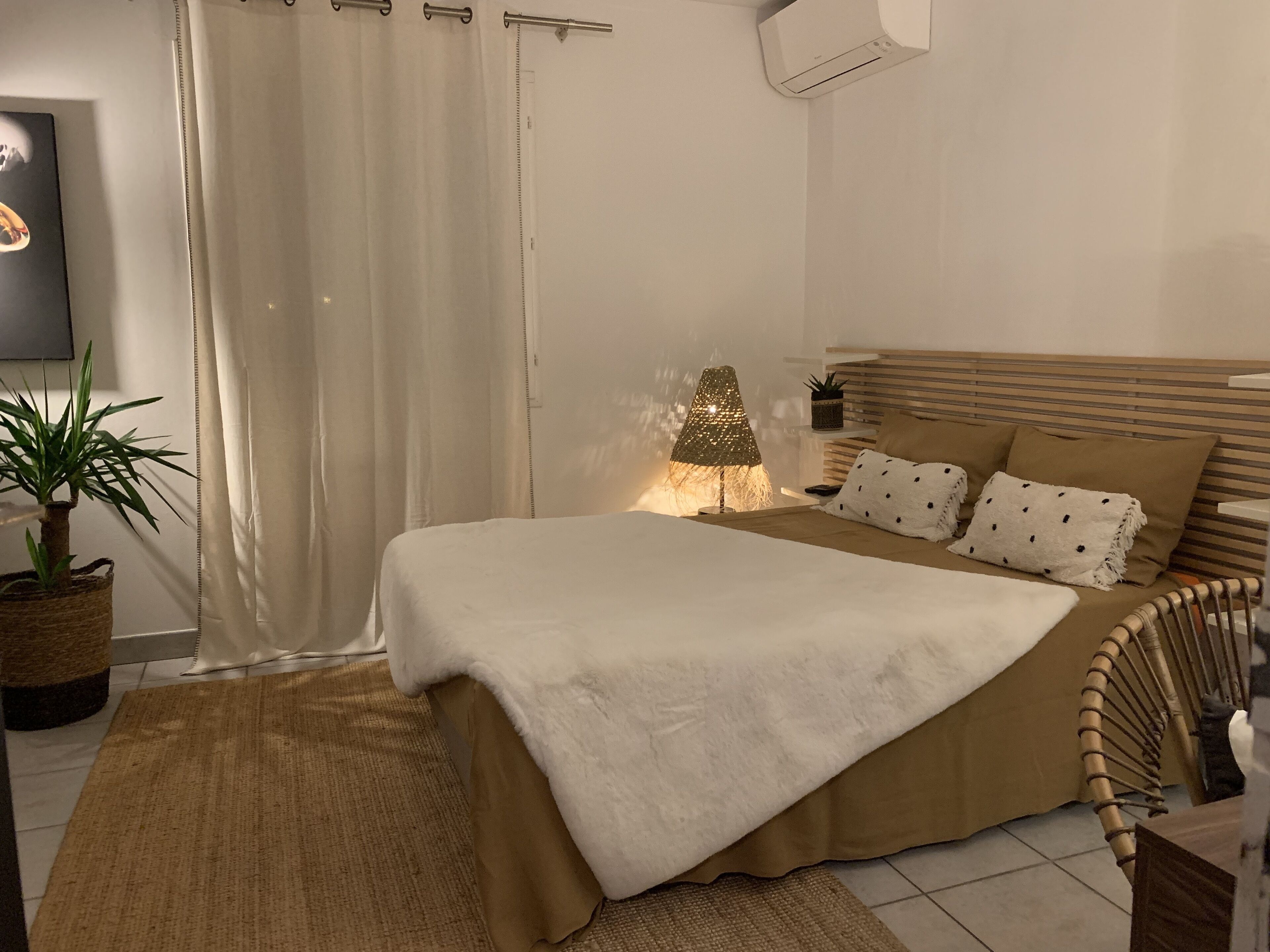 Een slaapkamer met een bed, een bedlamp, een potplant en een wandairconditioner.