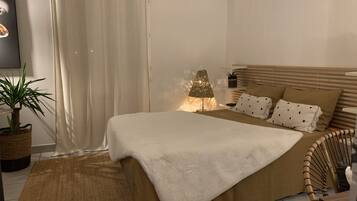 Een slaapkamer met een bed, een bedlamp, een potplant en een wandairconditioner.