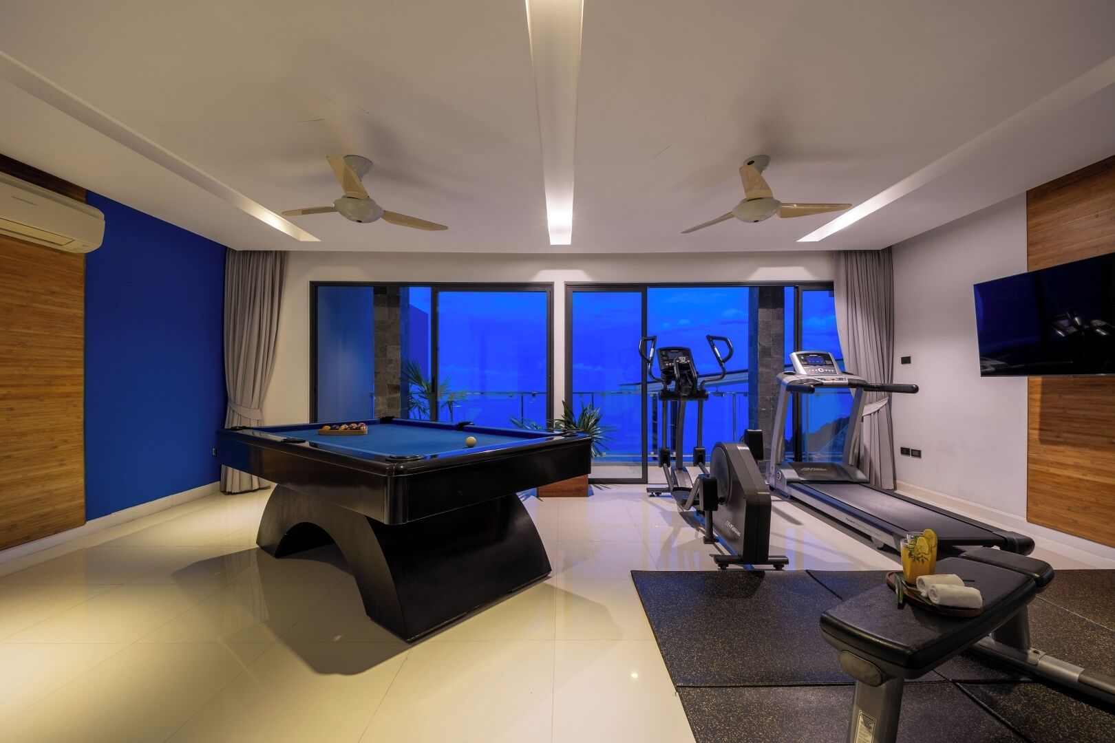 Een moderne kamer met een pooltafel, fitnessapparatuur en een groot raam met uitzicht.
