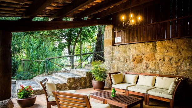 A covered patio with wooden furniture, a stone wall, and a view of greenery. - Casa Corral for 6 people (Lladurs)