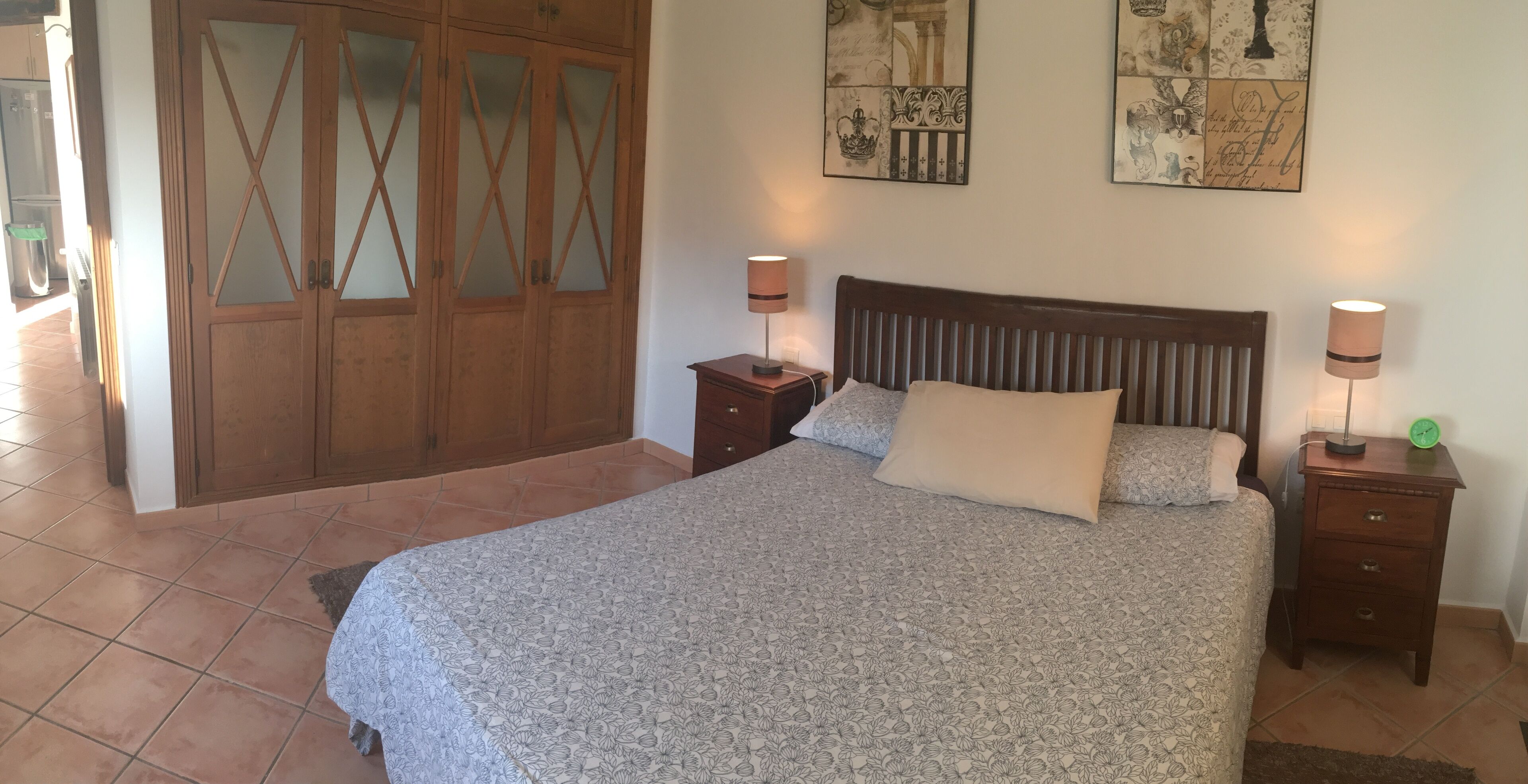 Une chambre à coucher comprenant un lit, deux tables de chevet, une armoire en bois et des œuvres d’art murales.