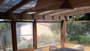 A covered patio with a table and chairs, large windows, and a view of greenery and a building. - Villa with sea access on foot!  Quiet and large shady garden (Sanary-Sur-Mer)