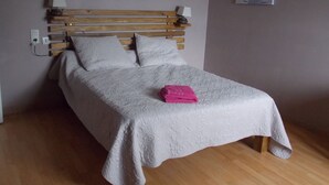 A neatly made bed with a wooden headboard, white bedding, and a pink towel.